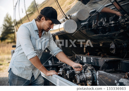 In shirt and in a cap. Truck driver is near the transport outdoors In shirt and in a cap. Truck driver is near the transport outdoors 133336983