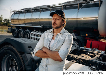 In shirt and in a cap. Truck driver is near the transport outdoors In shirt and in a cap. Truck driver is near the transport outdoors 133336997