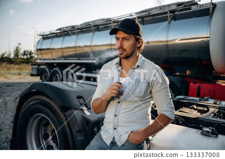 Smoking the electronic cigarette, vape. Truck driver is near the transport outdoors Smoking the electronic cigarette, vape. Truck driver is near the transport outdoors 133337008