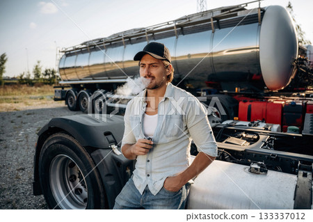 Smoking the electronic cigarette, vape. Truck driver is near the transport outdoors Smoking the electronic cigarette, vape. Truck driver is near the transport outdoors 133337012