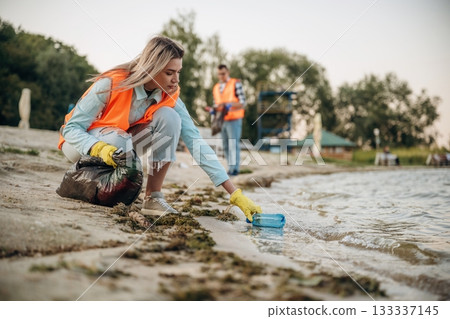 Picking bottle from the water. A volunteers collects garbage on a muddy beach Picking bottle from the water. A volunteers collects garbage on a muddy beach 133337145