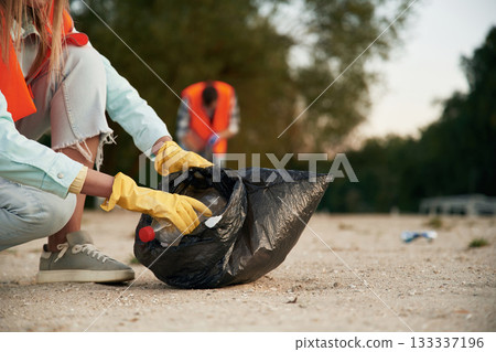 Picking up the bottle. A volunteers collects garbage on a muddy beach 133337196