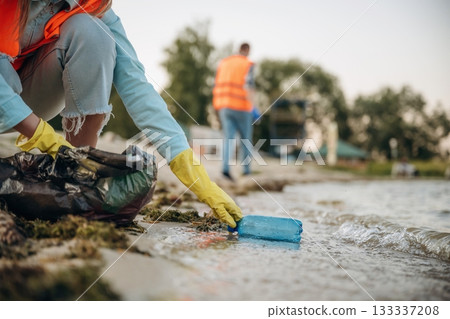 Picking bottle from the water. A volunteers collects garbage on a muddy beach 133337208