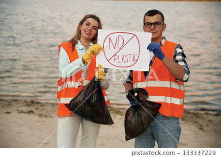 Poster with 'no plastic' text. A volunteers collects garbage on a muddy beach Poster with 'no plastic' text. A volunteers collects garbage on a muddy beach 133337229