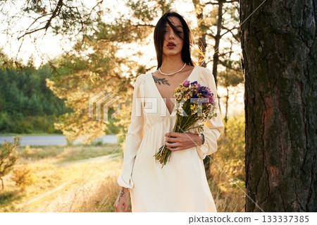 White dress. Bouquet in hands. Woman is outdoors in nature with bouquet of flowers 133337385