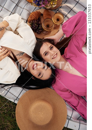 Top view, lying down. Lesbian couple is together on the picnic in nature Top view, lying down. Lesbian couple is together on the picnic in nature 133337653