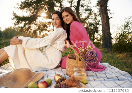 Sitting, bunch of fruits and flowers bouquet. Lesbian couple is together on the picnic in nature 133337683