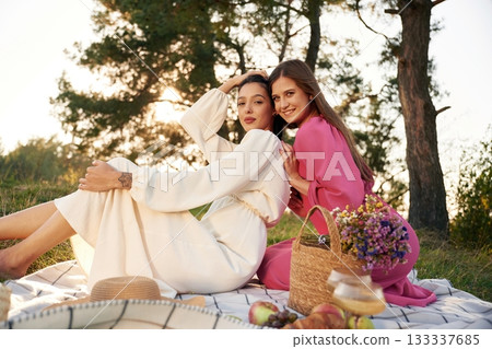 Sitting, bunch of fruits and flowers bouquet. Lesbian couple is together on the picnic in nature Sitting, bunch of fruits and flowers bouquet. Lesbian couple is together on the picnic in nature 133337685