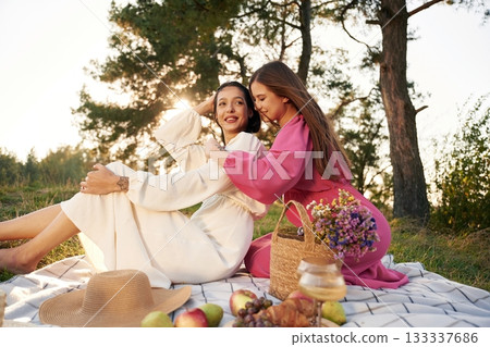 Sitting, bunch of fruits and flowers bouquet. Lesbian couple is together on the picnic in nature Sitting, bunch of fruits and flowers bouquet. Lesbian couple is together on the picnic in nature 133337686