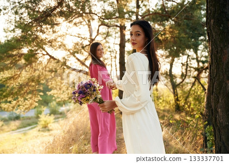 Woman is want to go, with bouquet of flowers. Lovely lesbian couple are together outdoors in nature Woman is want to go, with bouquet of flowers. Lovely lesbian couple are together outdoors in nature 133337701