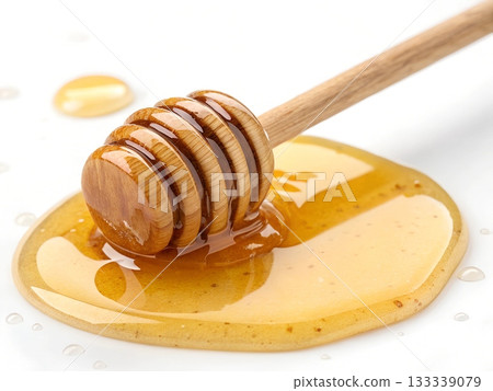 Wooden honey dipper resting in a pool of golden honey on a white background Wooden honey dipper resting in a pool of golden honey on a white background 133339079