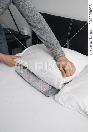 man placing his pajamas under his pillow man placing his pajamas under his pillow 133339608