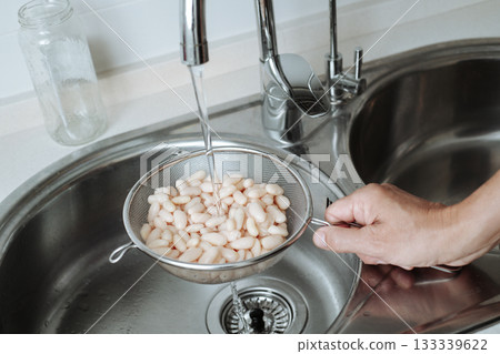 man rinses cooked white beans under tap water 133339622