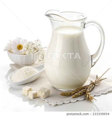 A glass pitcher filled with fresh milk sits beside white flowers cheese cubes and a spoon of milk powder 133339934