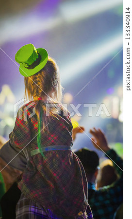 Little girl in green leprechaun hat sitting on shoulders at club during St. Patrick Day concert. Concept of Irish joy, family fun, shared festive tradition 133340914