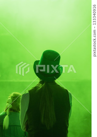 Back view of person in green top hat looking at hazy stage during St. Patrick Day event. Concept of mystery, folklore, immersive celebration Back view of person in green top hat looking at hazy stage during St. Patrick Day event. Concept of mystery, folklore, immersive celebration 133340916