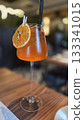 Aperol spritz with dried orange garnish on wooden table in cozy cafe setting. Vertical poster 133341015