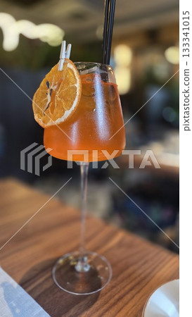 Aperol spritz with dried orange garnish on wooden table in cozy cafe setting. Vertical poster Aperol spritz with dried orange garnish on wooden table in cozy cafe setting. Vertical poster 133341015