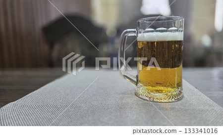 Refreshing mug of beer on a table in a cozy pub setting. Horizontal banner. Copy space. Free space for text. International beer day Refreshing mug of beer on a table in a cozy pub setting. Horizontal banner. Copy space. Free space for text. International beer day 133341016