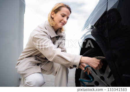 Woman inflating car tire at gas station using air pump Woman inflating car tire at gas station using air pump 133341583