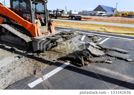 Construction work is underway as skid steer breaks up old asphalt in parking lot creating dust. Construction work is underway as skid steer breaks up old asphalt in parking lot creating dust. 133341636