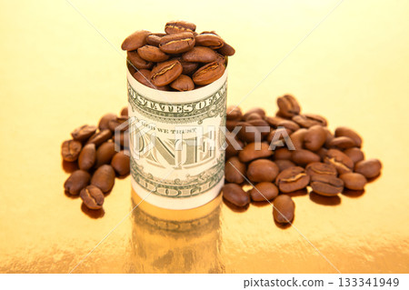A U.S. one-dollar bill, rolled into a tube, holds coffee beans on a golden surface 133341949