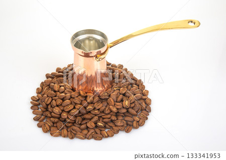 A shiny copper cezve with a brass handle alongside a pile of coffee beans A shiny copper cezve with a brass handle alongside a pile of coffee beans 133341953