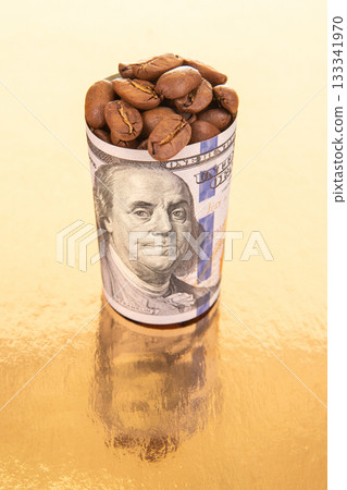 On a reflective gold surface, a rolled dollar bill filled with coffee beans 133341970
