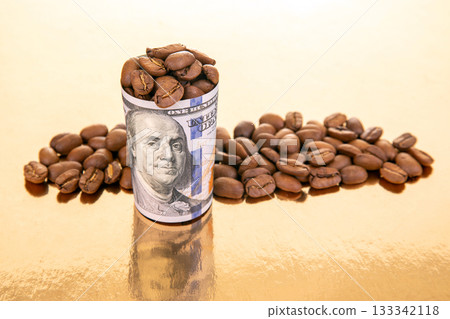 Coffee beans overflow from a rolled U.S. dollar bill on a golden reflective  133342118