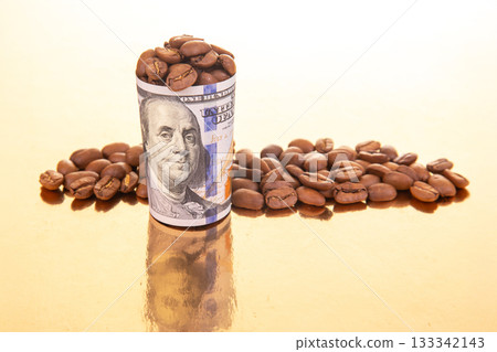 On a reflective gold surface, a rolled dollar bill filled with coffee beans  133342143