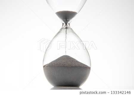 Minimalist hourglass with black sand trickling down on a white backdrop Minimalist hourglass with black sand trickling down on a white backdrop 133342146