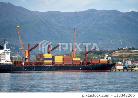 Commercial cargo ship waiting at terminal in sea port, cranes ready to load ship with containers. Commercial cargo ship waiting at terminal in sea port, cranes ready to load ship with containers. 133342200