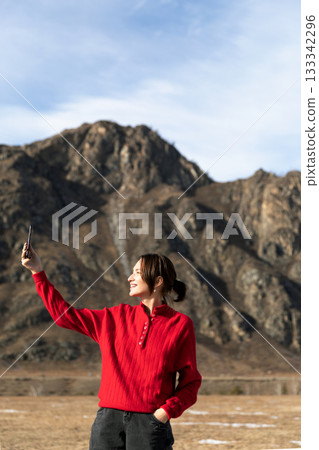 Woman in Red Sweater Capturing Scenic Mountain View with Phone Woman in Red Sweater Capturing Scenic Mountain View with Phone 133342296