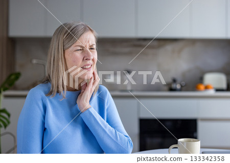 Mature woman feeling intense pain in her jaw or neck, touching her cheek and clenching her teeth, indicating discomfort and need for relief or medical attention Mature woman feeling intense pain in her jaw or neck, touching her cheek and clenching her teeth, indicating discomfort and need for relief or medical attention 133342358