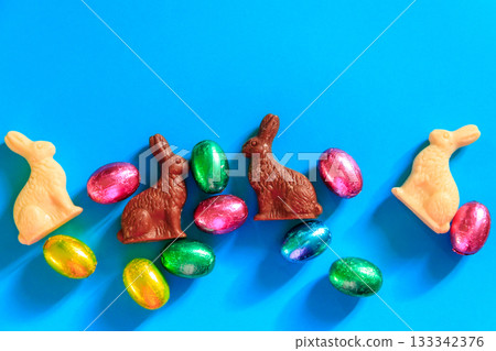 Easter chocolate eggs in foil and Easter chocolate bunnies on blue background. Top view 133342376
