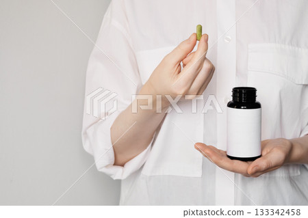 Woman holding green natural capsule and blank label vitamin bottle, promoting wellness Woman holding green natural capsule and blank label vitamin bottle, promoting wellness 133342458