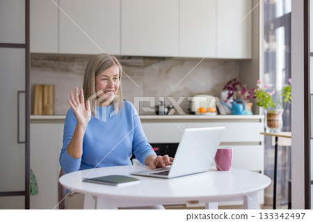 Senior woman actively engaging in a video call with a laptop from her home kitchen, enjoying modern communication technology to stay connected with family and friends Senior woman actively engaging in a video call with a laptop from her home kitchen, enjoying modern communication technology to stay connected with family and friends 133342497