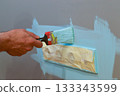 Using a brush to paint around an electrical socket on the wall, with masking tape applied for protection, as a DIY interior repair, aiming for precise results and safety. 133343599