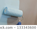A construction professional is applying a fresh coat of bright white paint to an interior wall using a roller brush, as part of an apartment renovation project. 133343600
