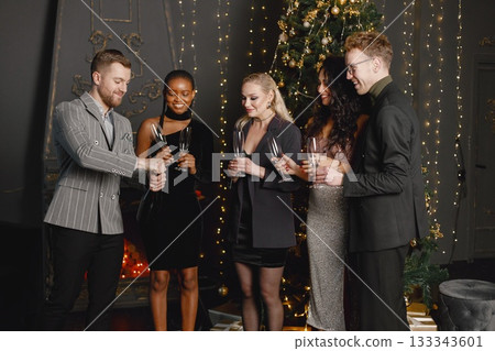 A pretty young women with a hairstyle in an elegant outfits and man in costumes holding a glasses with champagne. Women standing in the decorated interior of the house during the Christmas holiday and 133343601