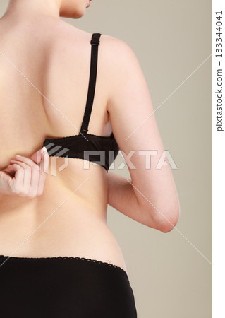 Woman dressing up her bra rear view 133344041