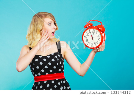 Shocked girl with alarm clock on blue. 133344312