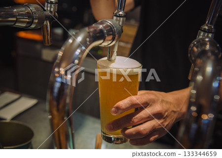 Draft beer being poured into a glass from a beer server 133344659