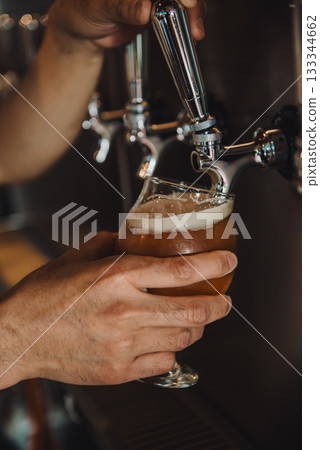 Close-up of a hand pouring draft beer from a tap into a round glass Close-up of a hand pouring draft beer from a tap into a round glass 133344662