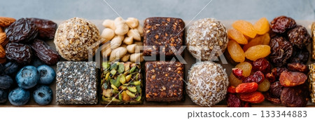 A variety of colorful energy balls and dried fruits are neatly arranged on a wooden board, ideal for healthy snacking 133344883
