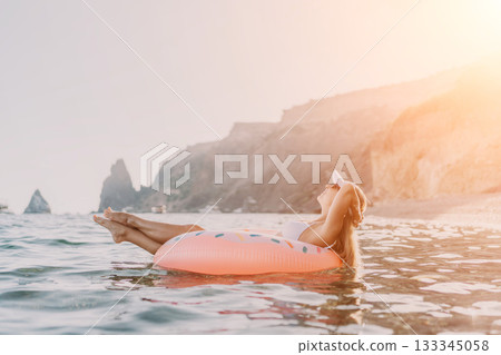 Woman float ocean, happy young woman relaxing on inflatable donut in calm sea with cliffs, summer vacation leisure. Woman float ocean, happy young woman relaxing on inflatable donut in calm sea with cliffs, summer vacation leisure. 133345058