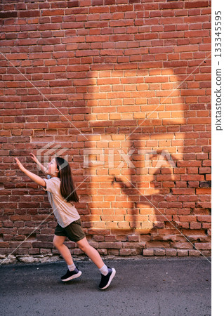 Child girl running chasing shadow on brick wall Child girl running chasing shadow on brick wall 133345595