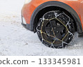 Chains on wheel of orange car in winter in outdoor. Vehicle equipment for off-road and bad weather. 133345981