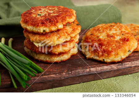 Crispy potato pancakes Latkes, stacked on a wooden board next to fresh green onions, natural light, homemade, no people, 133346054