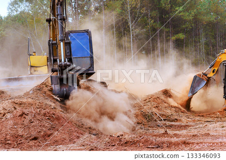 Heavy machines work to clear plot of land, creating dust clouds in forest landscape an active construction area 133346093